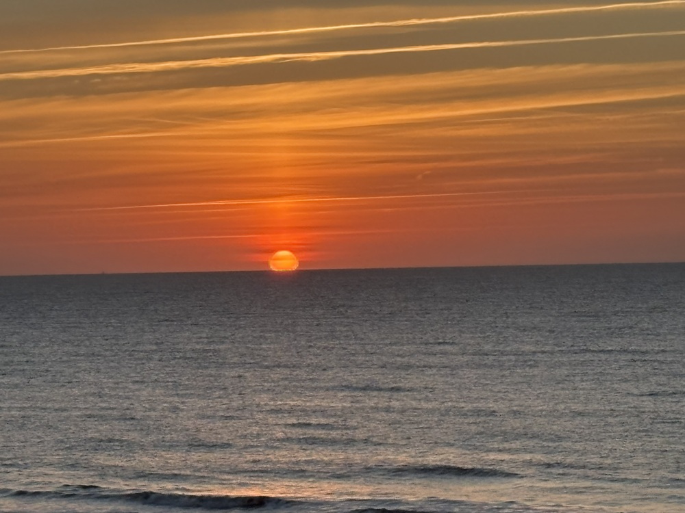 Craig Spiesman image showing the sun descending toward the ocean beneath orange clouds
